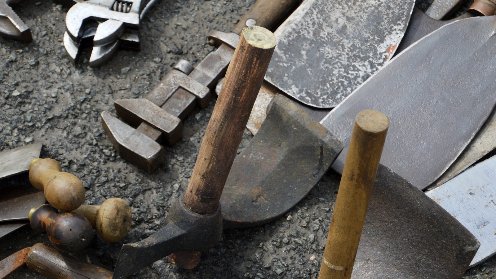 Gebrauchte Handwerkzeuge auf Schotterboden: Hämmer mit Holzgriffen, verstellbare Schraubenschlüssel und Schaufelblätter.