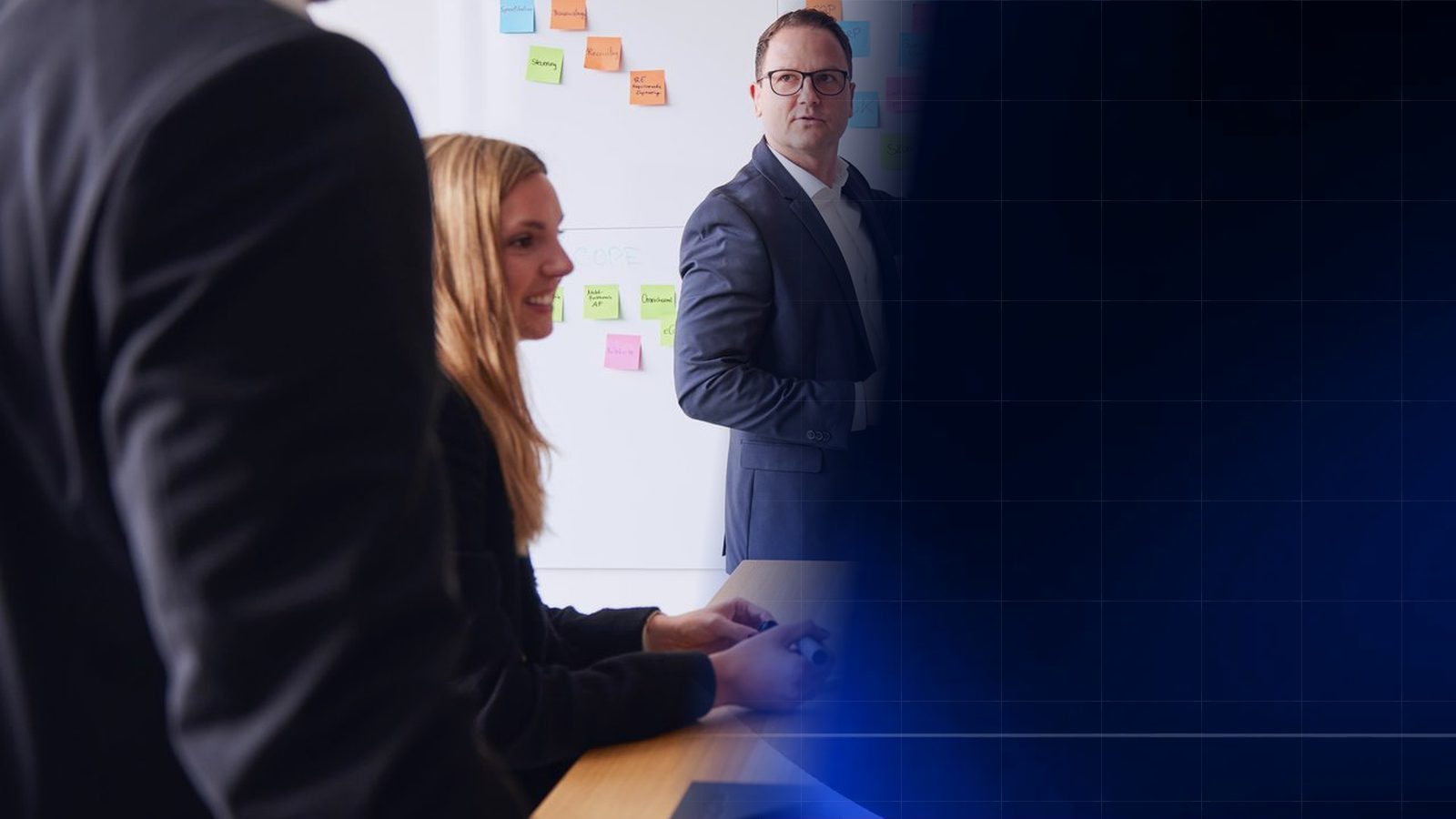 Workshop bei ReqPOOL: Ein Berater erläutert an einer Wand mit bunten Haftnotizen Prozesse und Systeme, eine Kollegin am Tisch und ein Kollege im Vordergrund hören zu; rechts geht das Bild in ein dunkelblaues Muster mit Rasterlinien über.