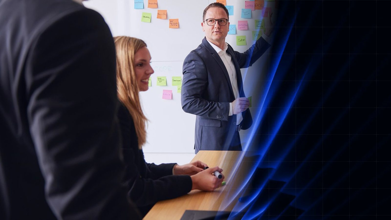 Workshop bei ReqPOOL: Ein Berater erläutert vor einer Wand mit Haftnotizen, eine Kollegin und ein Kollege hören am Tisch zu; rechts geht das Bild in abstrakte blaue Formen über.