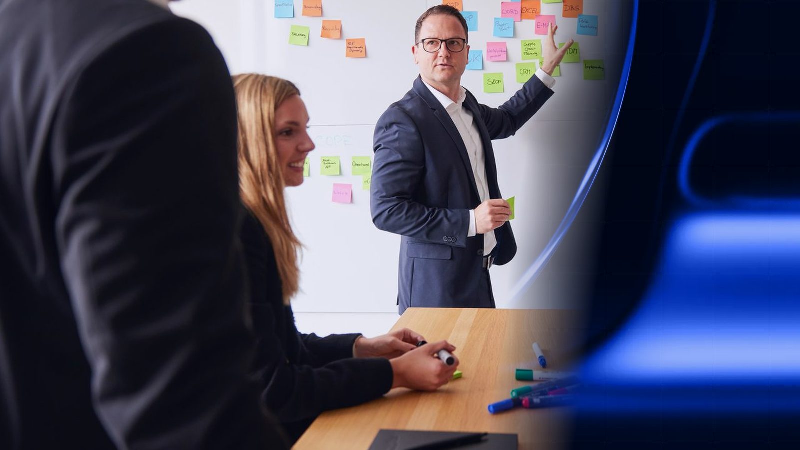 Workshop bei ReqPOOL: Ein Berater erläutert an einer Wand mit Haftnotizen eine Systemlandschaft, eine Kollegin und ein Kollege hören zu; rechts geht das Bild in eine blaue Fläche mit Rasterlinien über.