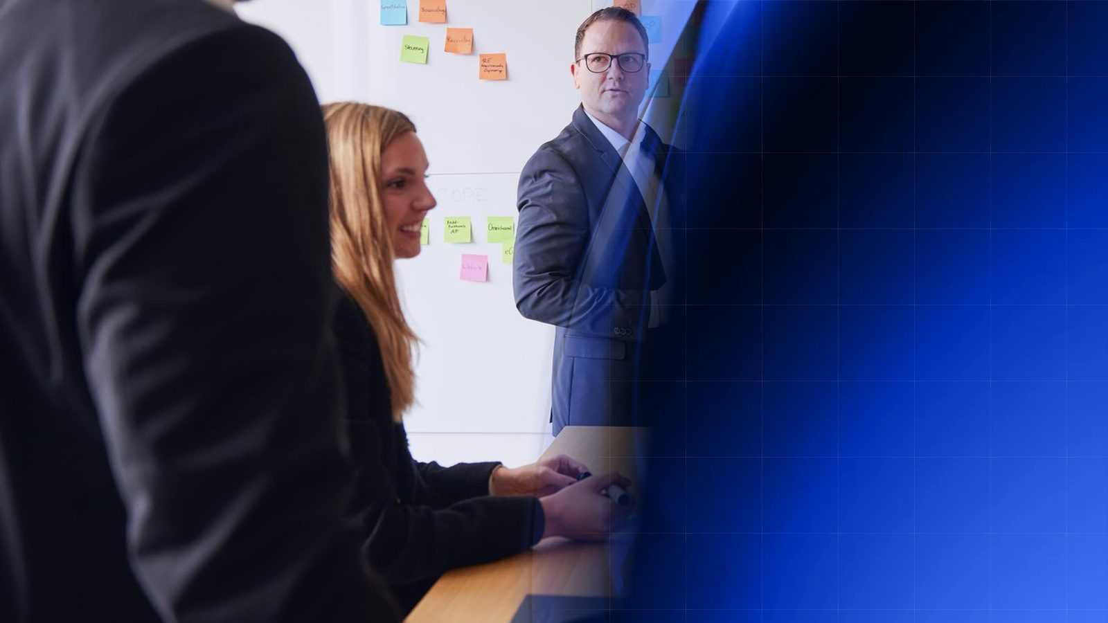 Workshop bei ReqPOOL: Ein Berater erläutert an einer Wand mit bunten Haftnotizen zu Prozessen und Systemen, eine Kollegin sitzt mit Stiften am Tisch, ein Kollege hört im Vordergrund zu; rechts geht das Bild in blaue geometrische Formen über.