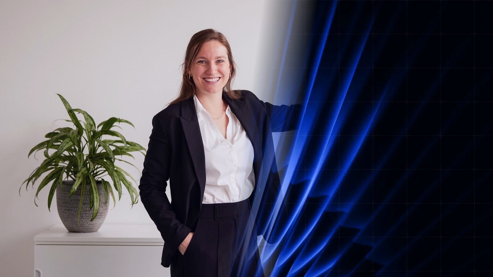 Eine ReqPOOL-Beraterin steht in einem hellen Büro neben einer Grünpflanze und weist mit dem Arm auf eine blaue Grafikfläche mit geschwungenen Formen.