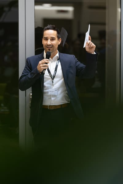 Moderator mit Mikrofon in einer Glastür hält ein Blatt Papier hoch