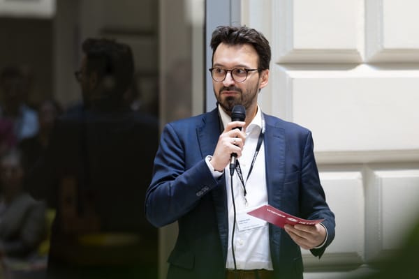 Redner mit Brille und Mikrofon hält ein rotes Kärtchen in der Hand