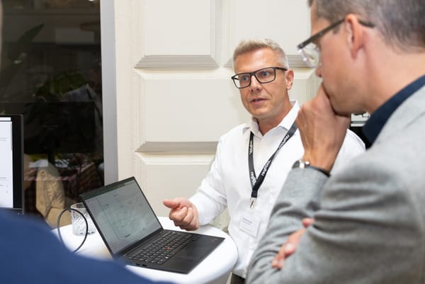 Gast erklärt an einem Stehtisch mit Laptop einem zweiten Gast etwas