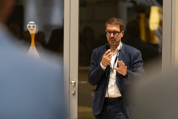 Redner gestikuliert beim Sprechen mit Mikrofon in einer Glastür