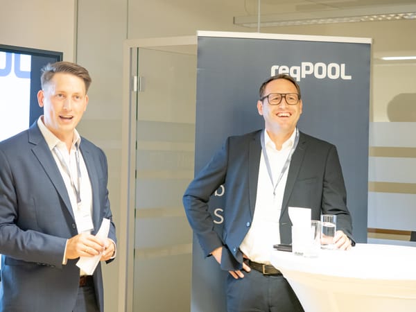 Zwei Männer in Anzügen sprechen vor einem ReqPOOL-Banner zu den Gästen