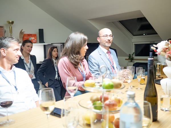 Gäste im Gespräch am langen Tisch mit Obst, Wein und Wasser