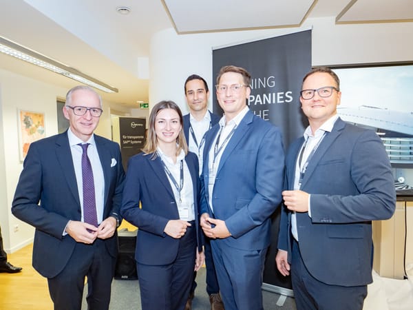 Fünf Personen in Business-Kleidung posieren vor einem Veranstaltungsbanner
