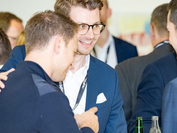 Zwei Gäste begrüßen sich herzlich, einer legt dem anderen den Arm um die Schulter