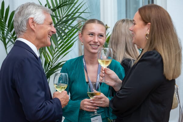 Drei Personen mit Weingläsern lachen im Gespräch zwischen Zimmerpflanzen